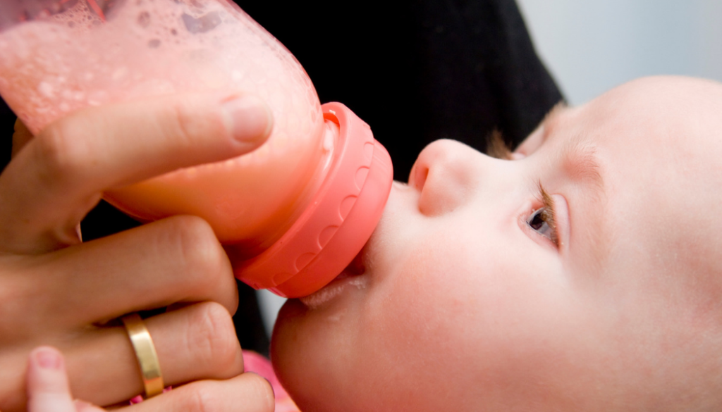 Ребенок ест кашу из бутылочки.